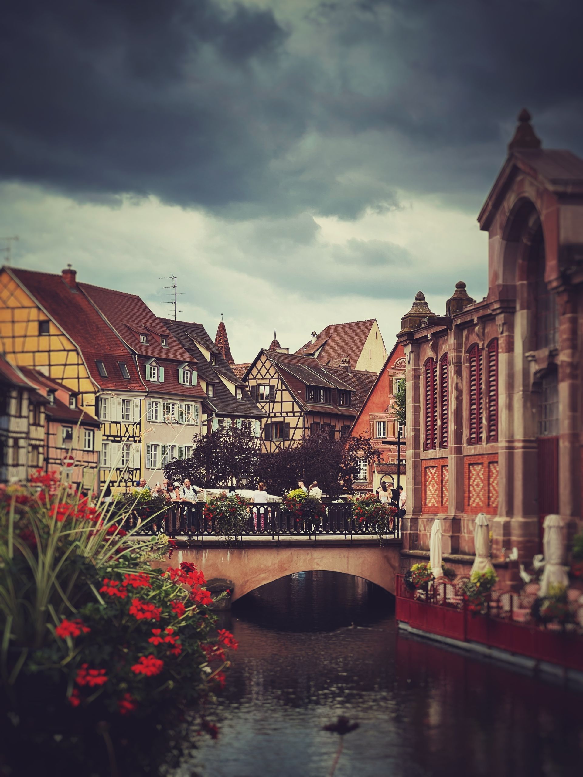 Picturesque canal view with historical buildings and bridge under dramatic sky.